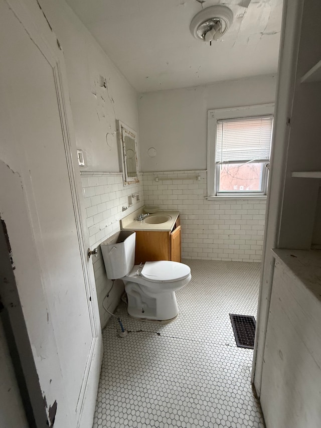 bathroom featuring visible vents, toilet, a wainscoted wall, a sink, and tile walls