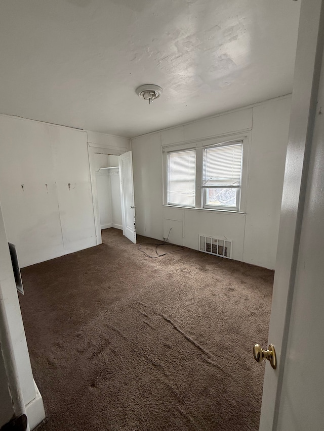 unfurnished bedroom with dark colored carpet, a closet, and visible vents