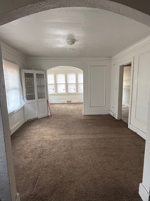 empty room with visible vents, dark colored carpet, and a decorative wall