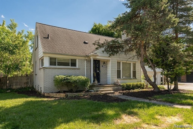 cape cod house with roof with shingles, brick siding, a front lawn, and fence