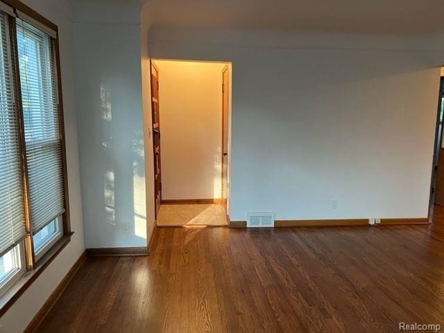 empty room featuring wood finished floors, visible vents, and baseboards