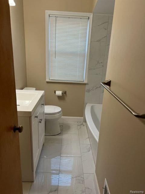 bathroom featuring baseboards, toilet, marble finish floor, a bathtub, and vanity