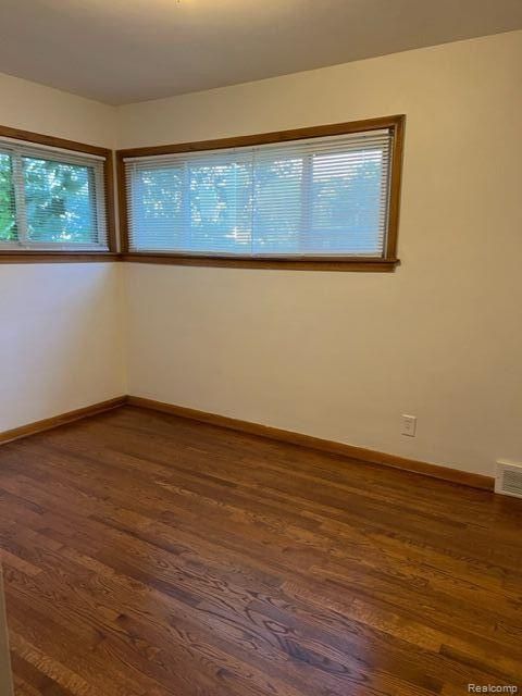 empty room with baseboards, visible vents, and dark wood-style flooring