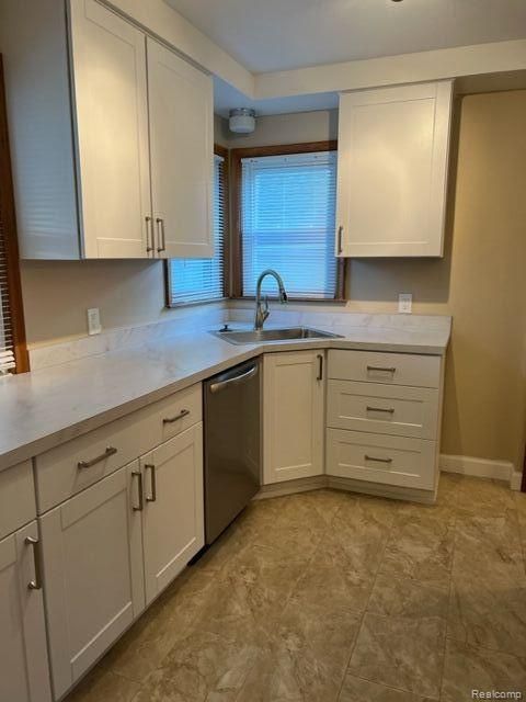 kitchen with light countertops, stainless steel dishwasher, white cabinets, a sink, and baseboards