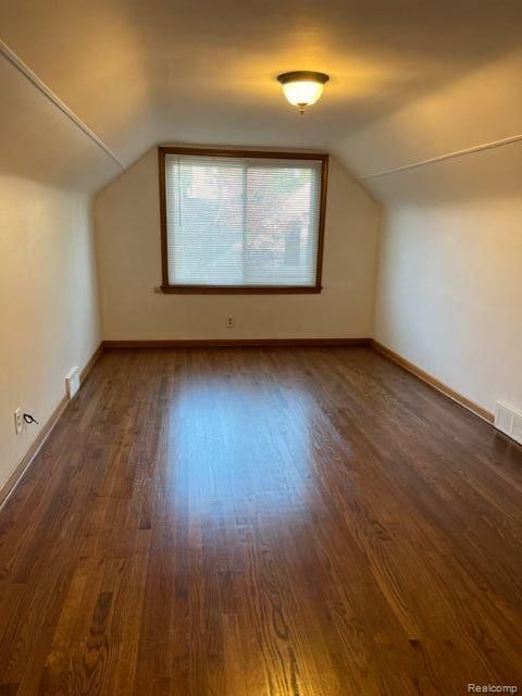 additional living space with lofted ceiling, baseboards, visible vents, and wood finished floors