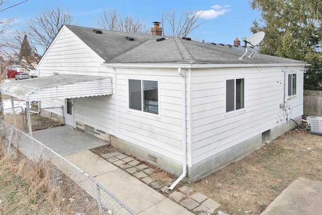 view of side of property featuring central AC unit, a shingled roof, fence, crawl space, and a chimney