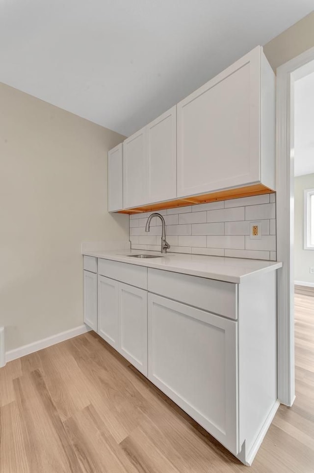 kitchen with baseboards, backsplash, light countertops, light wood-type flooring, and a sink