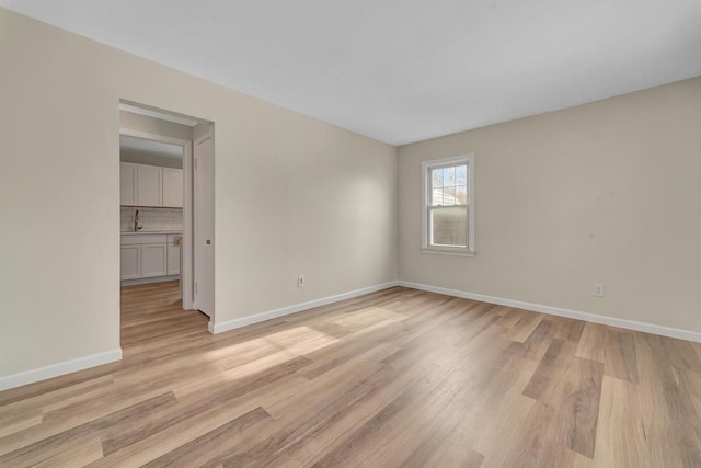 spare room with light wood-type flooring, a sink, and baseboards