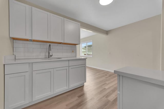 kitchen featuring light wood finished floors, light countertops, decorative backsplash, a sink, and baseboards