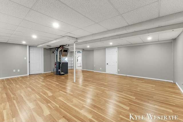 finished basement featuring a drop ceiling, light wood-type flooring, heating unit, and baseboards