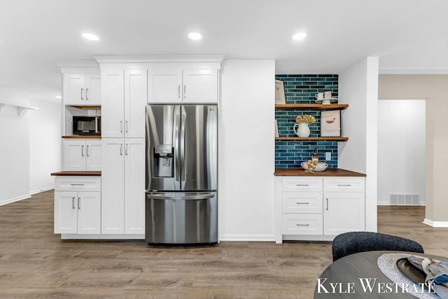 kitchen featuring black microwave, visible vents, light wood-style floors, stainless steel refrigerator with ice dispenser, and backsplash