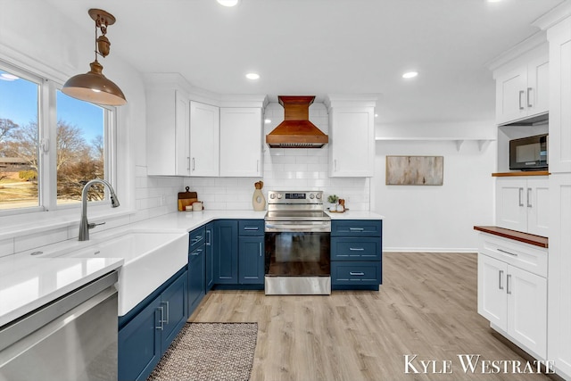 kitchen with white cabinets, blue cabinetry, appliances with stainless steel finishes, custom exhaust hood, and tasteful backsplash