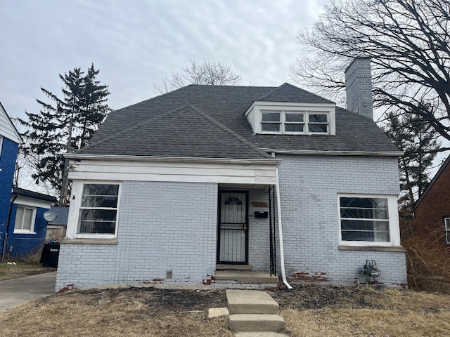 view of front facade featuring roof with shingles, a chimney, and brick siding