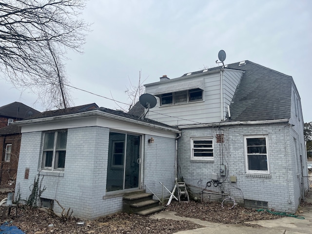 back of property with entry steps, a chimney, roof with shingles, crawl space, and brick siding