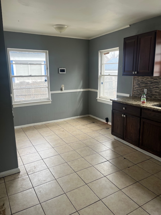 kitchen with dark brown cabinetry, stone countertops, baseboards, wainscoting, and backsplash