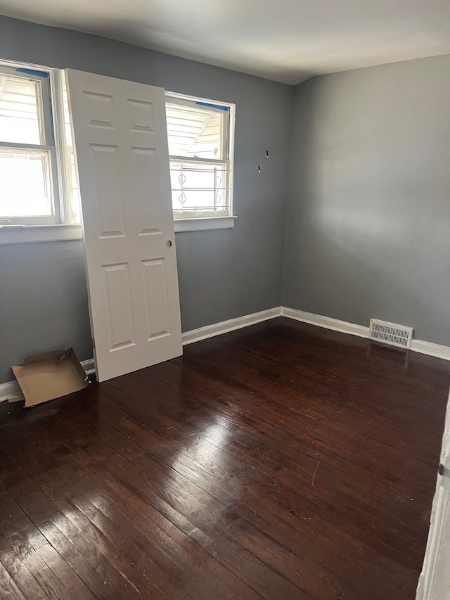 spare room with dark wood-style floors, visible vents, and baseboards