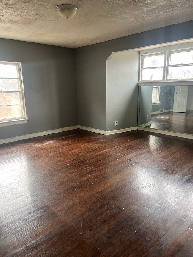 spare room with dark wood-style floors, a textured ceiling, and baseboards