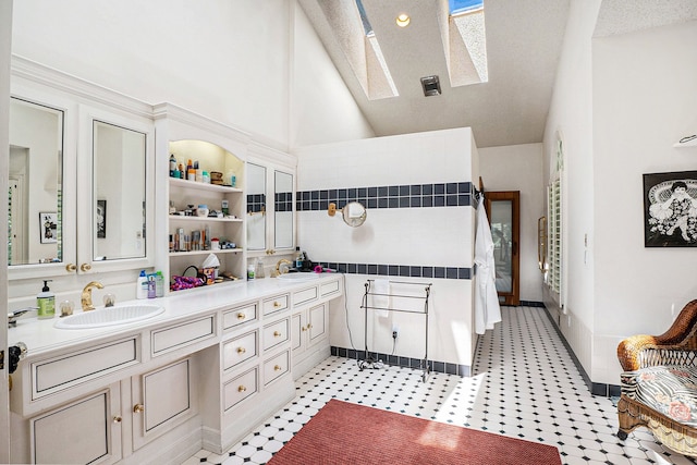 full bath featuring double vanity, vaulted ceiling with skylight, and a sink