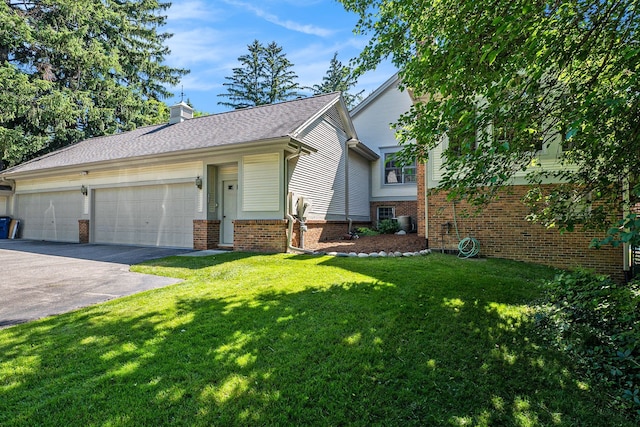 view of front of house with a garage, a chimney, aphalt driveway, a front yard, and brick siding