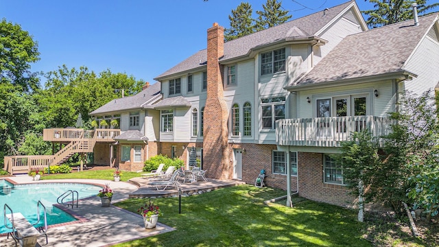 rear view of property featuring a deck, brick siding, a lawn, an outdoor pool, and a chimney