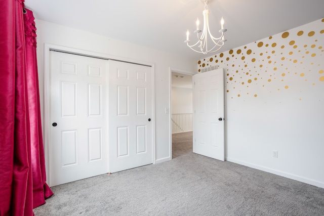 unfurnished bedroom with a closet, baseboards, an inviting chandelier, and carpet floors