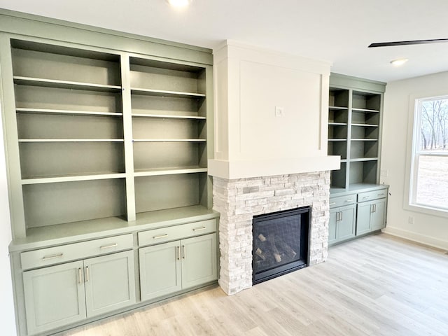 unfurnished living room featuring built in features, light wood-type flooring, a stone fireplace, and baseboards