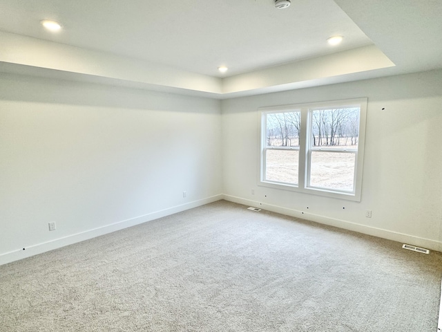 carpeted spare room featuring a tray ceiling, recessed lighting, visible vents, and baseboards