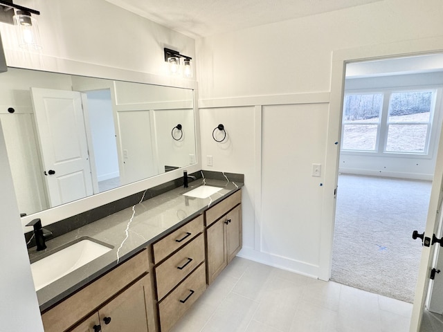 full bathroom with double vanity, a wainscoted wall, a decorative wall, and a sink