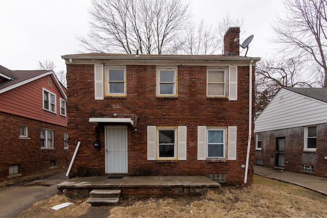 colonial home featuring brick siding, a patio, and a chimney