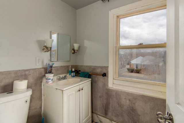 half bathroom featuring a wainscoted wall, toilet, vanity, and tile walls