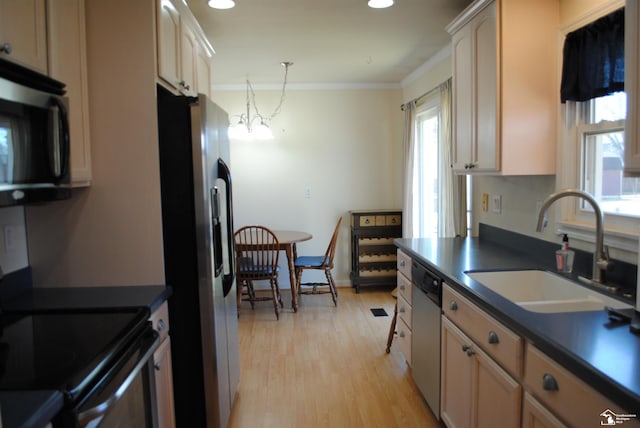 kitchen with a sink, appliances with stainless steel finishes, light wood-type flooring, dark countertops, and crown molding