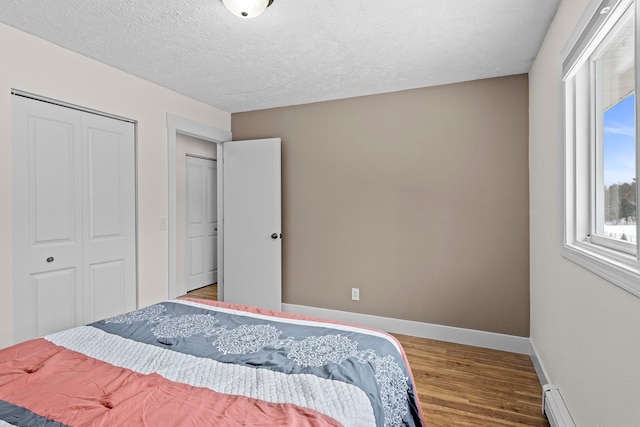 bedroom with a closet, baseboards, baseboard heating, and wood finished floors