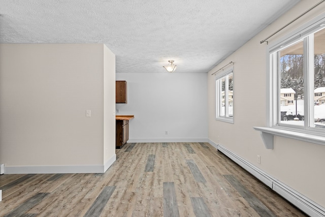 unfurnished room featuring light wood-style floors, baseboards, baseboard heating, and a textured ceiling