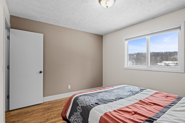 bedroom featuring light wood-style flooring, baseboards, and a textured ceiling