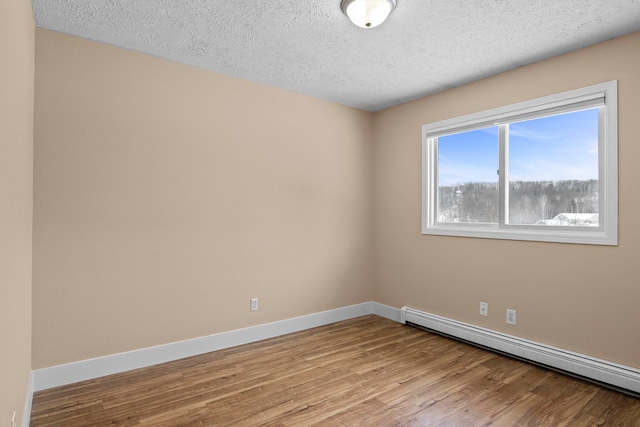 empty room with a textured ceiling, a baseboard radiator, wood finished floors, and baseboards