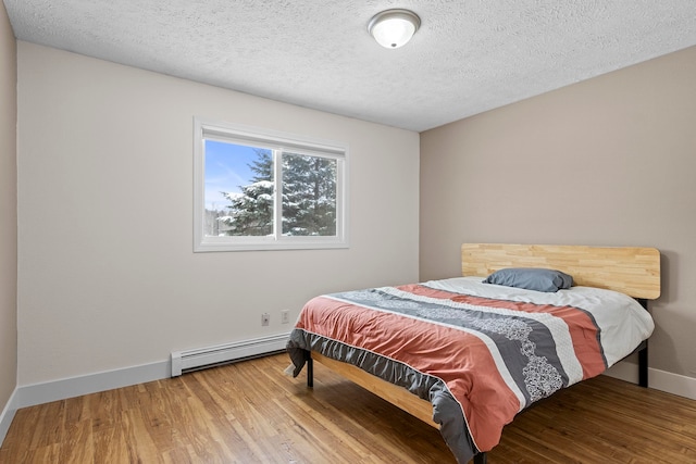 bedroom with a baseboard radiator, a textured ceiling, baseboards, and wood finished floors