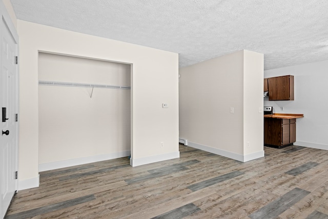 unfurnished bedroom with a textured ceiling, a closet, baseboards, and wood finished floors