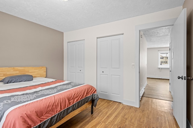 bedroom with baseboards, baseboard heating, a textured ceiling, light wood-style floors, and multiple closets