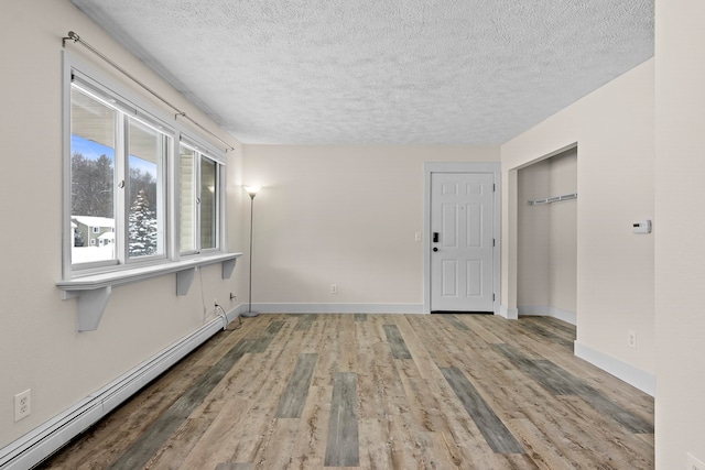 empty room featuring baseboards, a textured ceiling, a baseboard heating unit, and wood finished floors