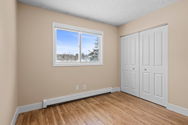 unfurnished bedroom featuring a textured ceiling, baseboards, light wood-style floors, baseboard heating, and a closet