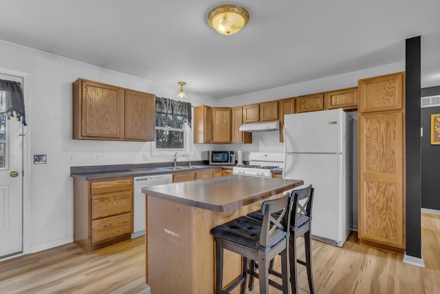 kitchen featuring white appliances, dark countertops, light wood-style flooring, a breakfast bar area, and under cabinet range hood