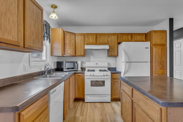 kitchen featuring white appliances, dark countertops, light wood-type flooring, under cabinet range hood, and a sink