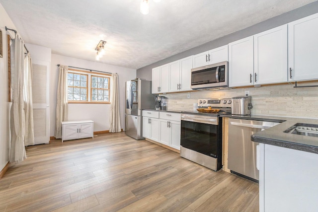 kitchen with stainless steel appliances, white cabinets, light wood-type flooring, tasteful backsplash, and dark countertops