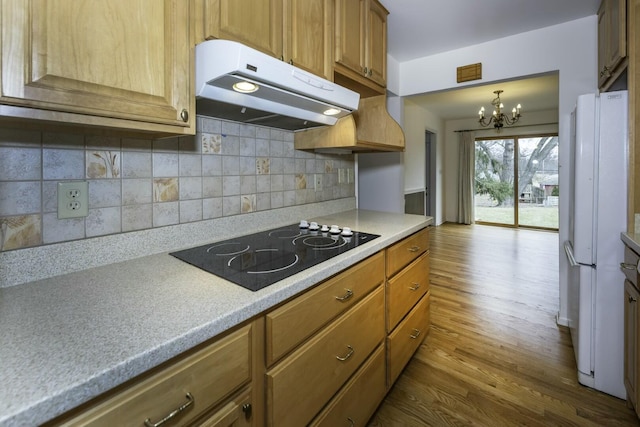 kitchen with dark wood-type flooring, freestanding refrigerator, black electric stovetop, light countertops, and under cabinet range hood