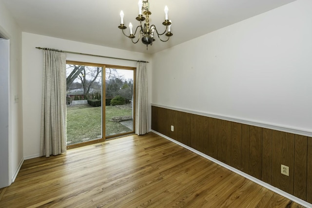 unfurnished dining area with a wainscoted wall, wood finished floors, visible vents, and an inviting chandelier