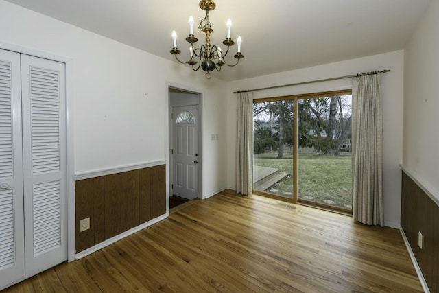 unfurnished dining area featuring visible vents, an inviting chandelier, wainscoting, wood walls, and wood finished floors