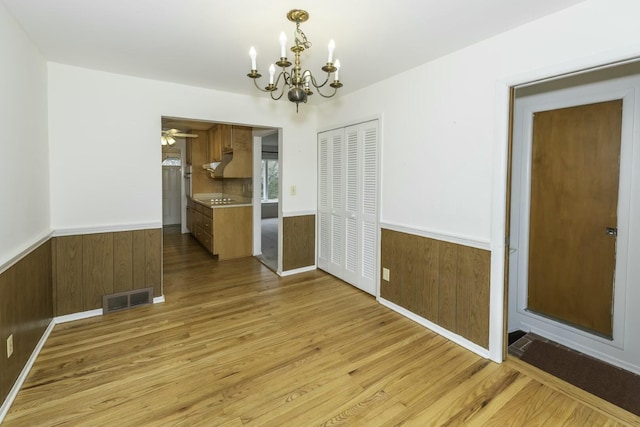 unfurnished dining area featuring a wainscoted wall, visible vents, wood walls, and light wood-style flooring