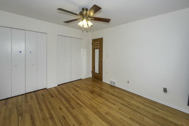 unfurnished bedroom with ceiling fan, visible vents, multiple closets, and wood finished floors