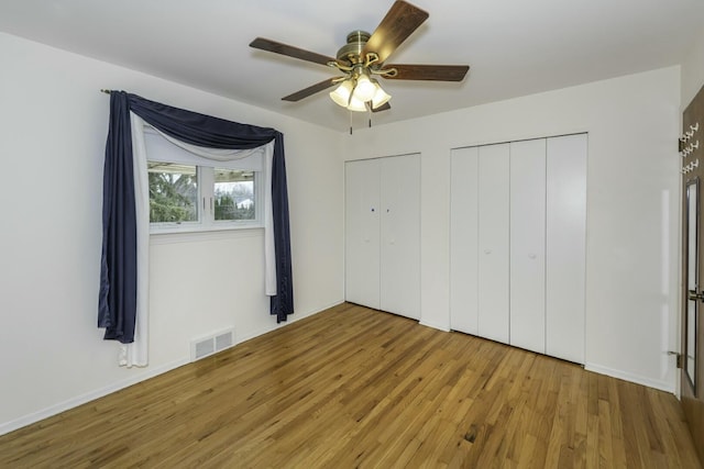 unfurnished bedroom with ceiling fan, two closets, wood finished floors, and visible vents