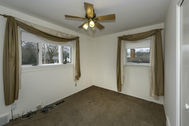 empty room featuring a ceiling fan, a healthy amount of sunlight, and dark carpet